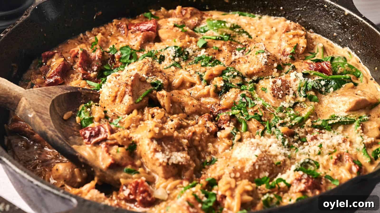 35 Chicken Breast Recipes to Simplify Weeknight Dinners 10 A skillet with creamy chicken pasta featuring spinach, sun-dried tomatoes, and grated cheese, stirred with a wooden spoon.