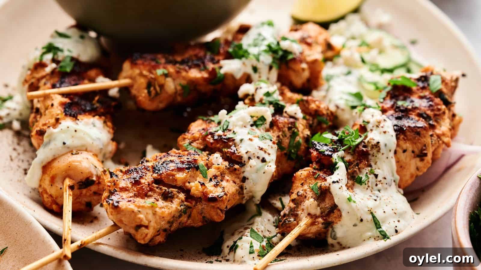 35 Chicken Breast Recipes to Simplify Weeknight Dinners 16 Grilled chicken skewers topped with a creamy white sauce and chopped herbs, served on a plate with sliced vegetables.