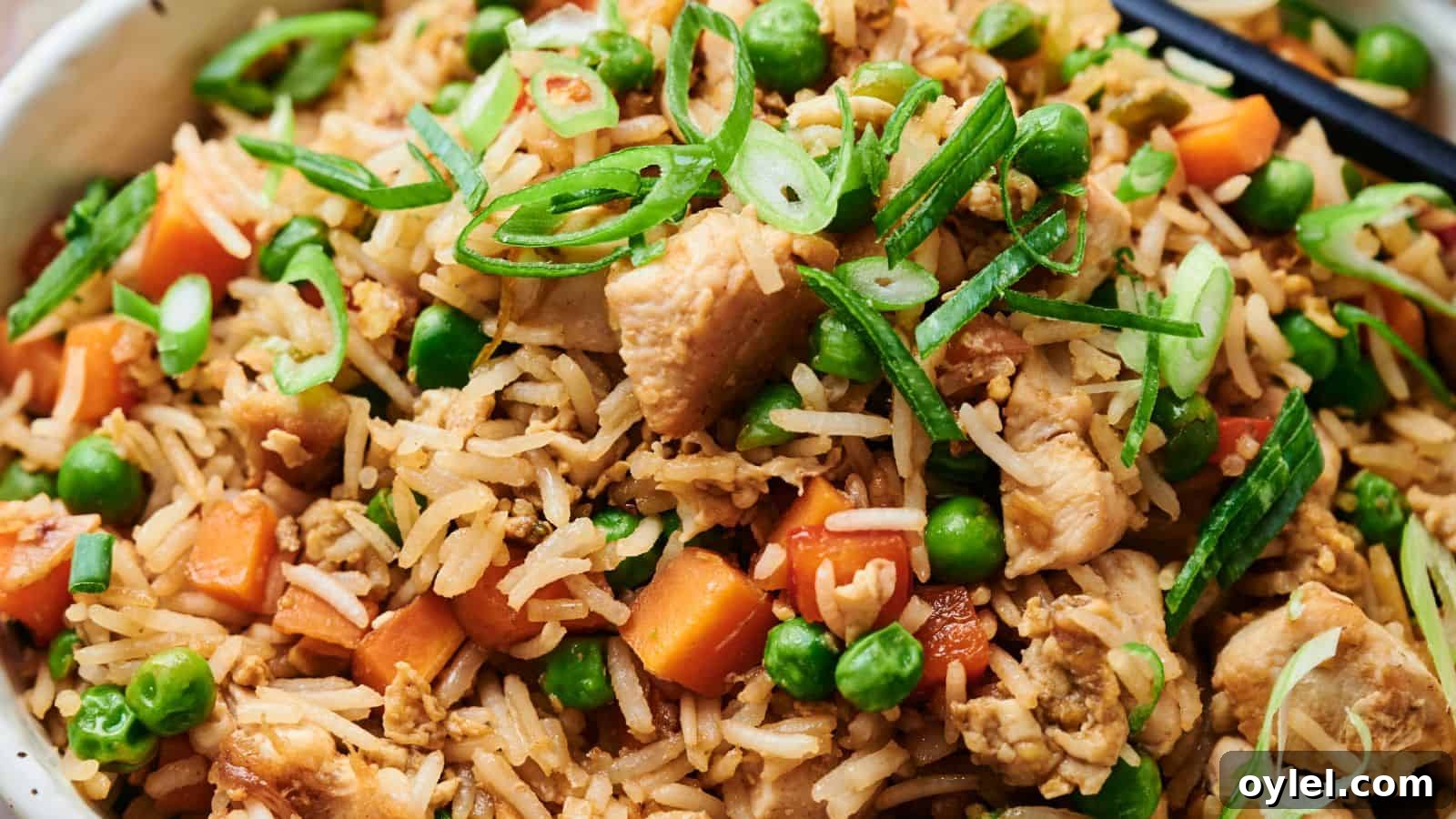35 Chicken Breast Recipes to Simplify Weeknight Dinners 18 Close-up of chicken fried rice with peas, carrots, sliced green onions, and chopsticks.