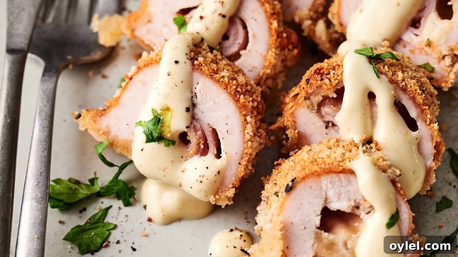 35 Chicken Breast Recipes to Simplify Weeknight Dinners 19 Sliced breaded chicken rolls filled with ham and cheese, topped with creamy sauce and garnished with chopped parsley on a plate.