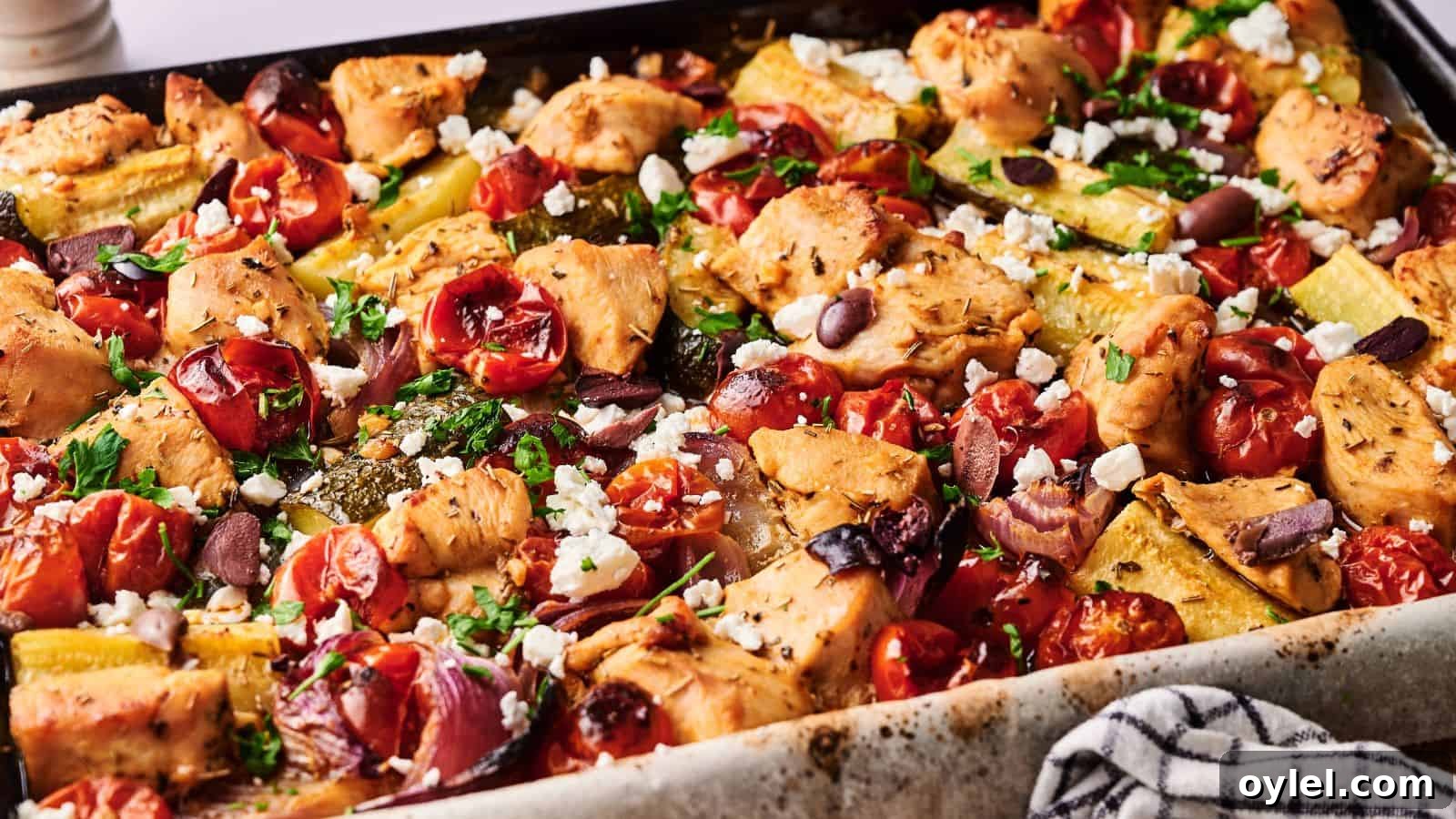 35 Chicken Breast Recipes to Simplify Weeknight Dinners 22 Sheet pan filled with baked chicken pieces, cherry tomatoes, zucchini, olives, and crumbled feta cheese, garnished with herbs.