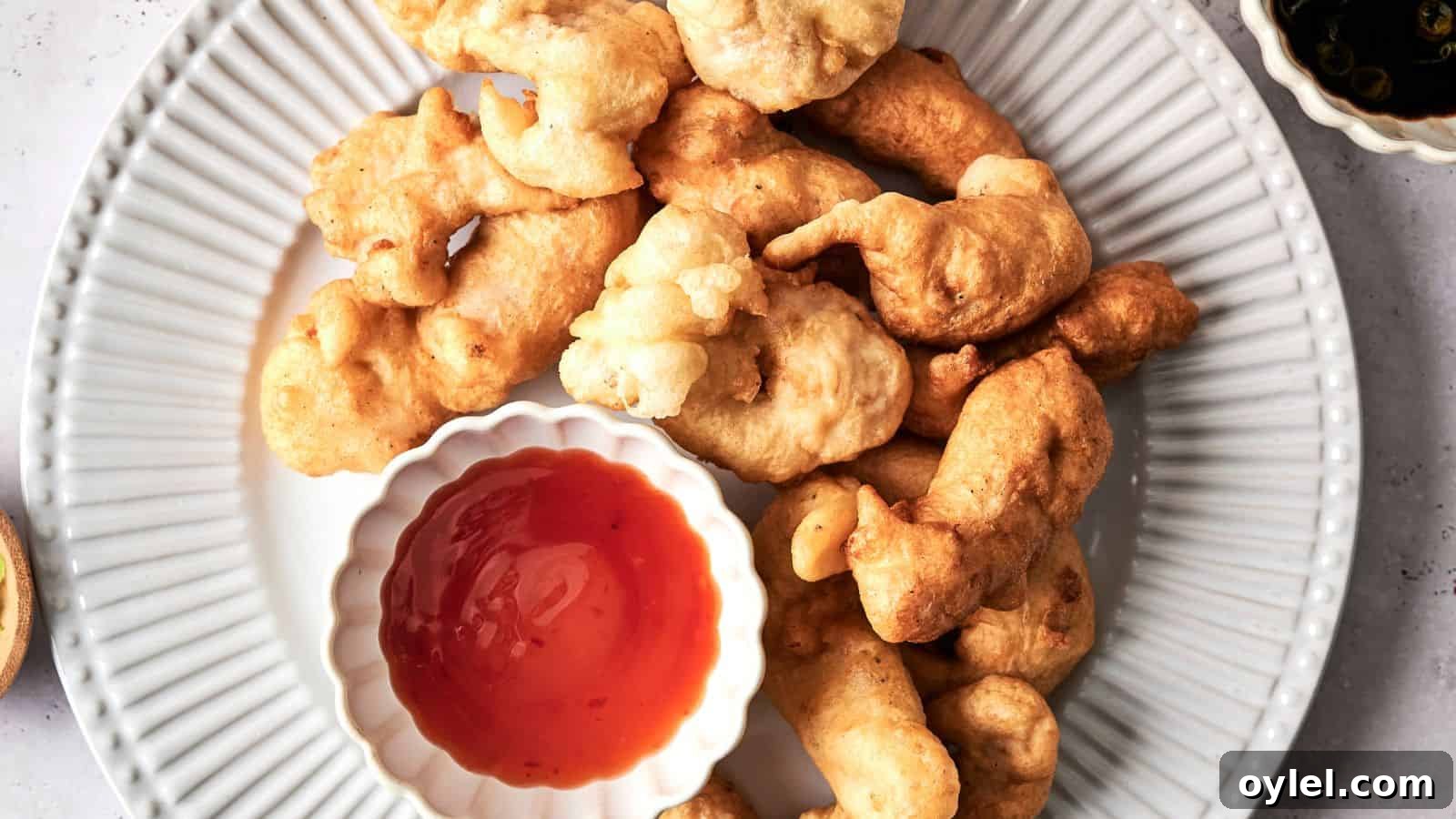 35 Chicken Breast Recipes to Simplify Weeknight Dinners 25 Plate of batter-fried fritters with a bowl of red dipping sauce on a white plate, viewed from above.