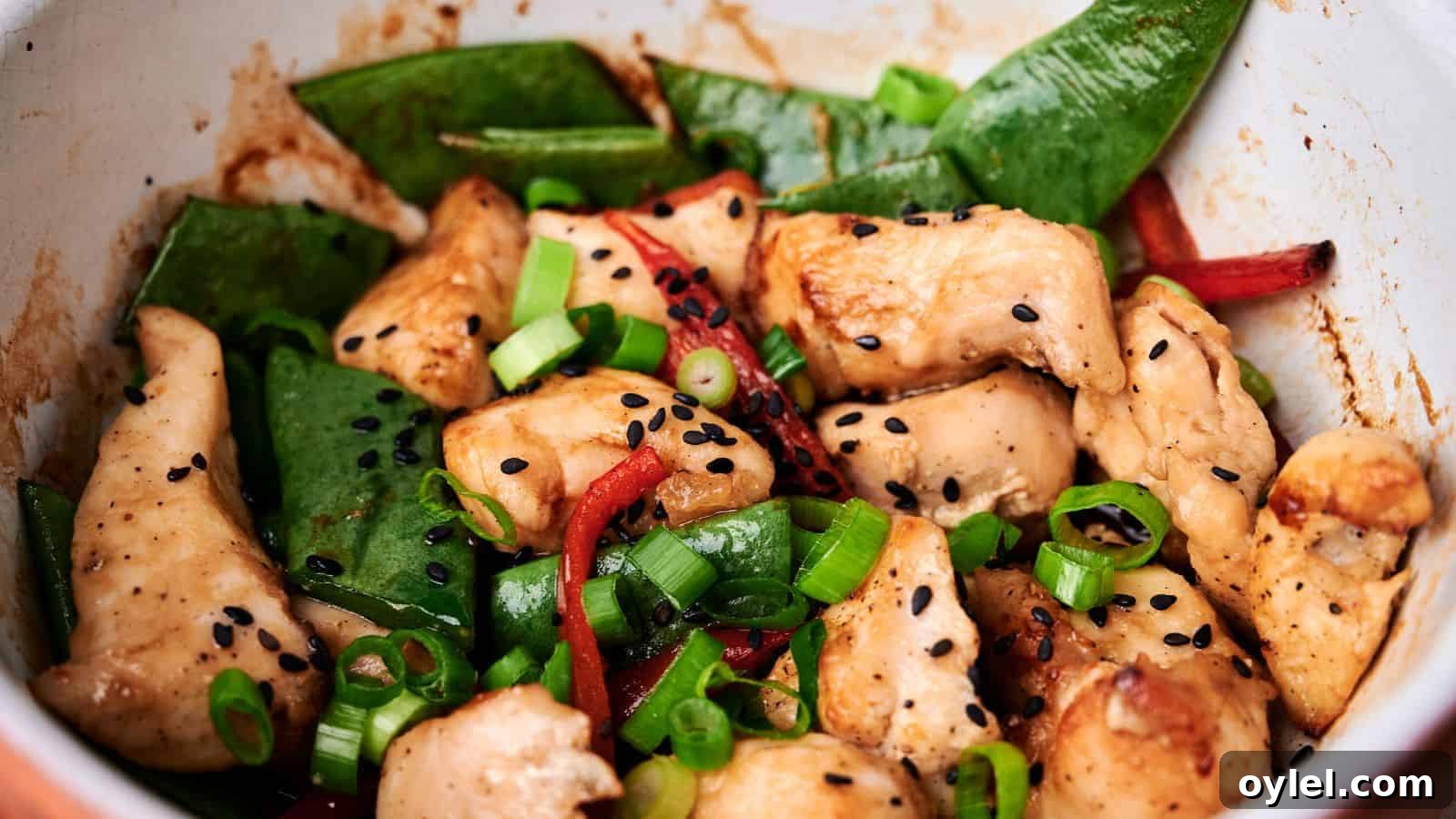 35 Chicken Breast Recipes to Simplify Weeknight Dinners 27 A close-up of a stir-fry dish featuring pieces of chicken, snap peas, red bell peppers, scallions, and black sesame seeds.