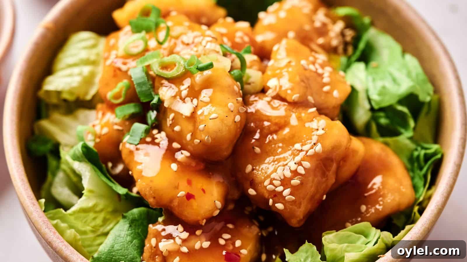 35 Chicken Breast Recipes to Simplify Weeknight Dinners 30 A bowl of crispy tofu coated in sesame sauce, garnished with green onions and sesame seeds, served on a bed of lettuce.