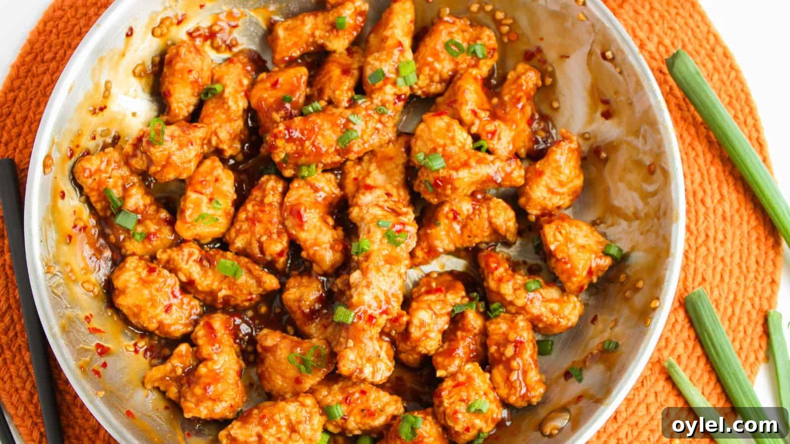35 Chicken Breast Recipes to Simplify Weeknight Dinners 8 Stir-fried chicken pieces in a spicy sauce, garnished with chopped green onions, served in a round metal dish on an orange placemat.