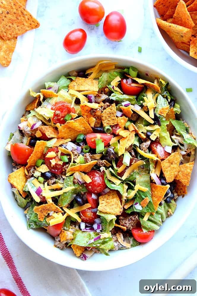 Dorito Taco Salad Recipe - chopped lettuce, tomatoes, seasoned meat, black beans, onions, zesty dressing and crunchy tortilla chips is everything you love about tacos in one tasty salad! Overhead shot of taco salad with tortilla chips, tomatoes, cheese and beans.