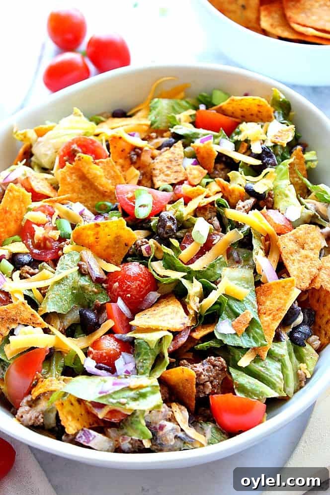 Dorito Taco Salad Recipe - chopped lettuce, tomatoes, seasoned meat, black beans, onions, zesty dressing and crunchy tortilla chips is everything you love about tacos in one tasty salad! Close up shot of Dorito taco salad in white bowl.