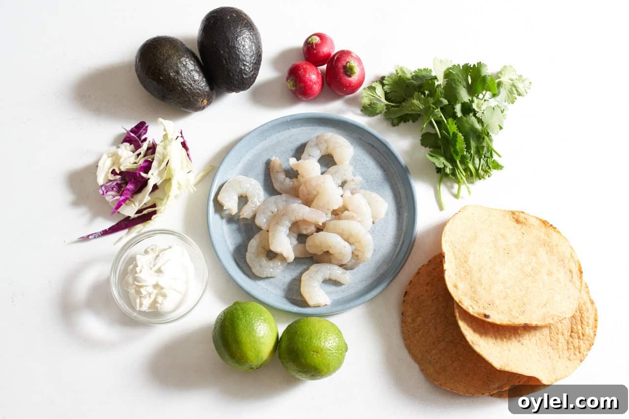 Crispy Mexican Shrimp Tostadas with Avocado Crema 3 A plate of raw shrimp surrounded by tostada shells, limes, chopped cabbage, cilantro, radishes, avocado, and a small bowl of sour cream.