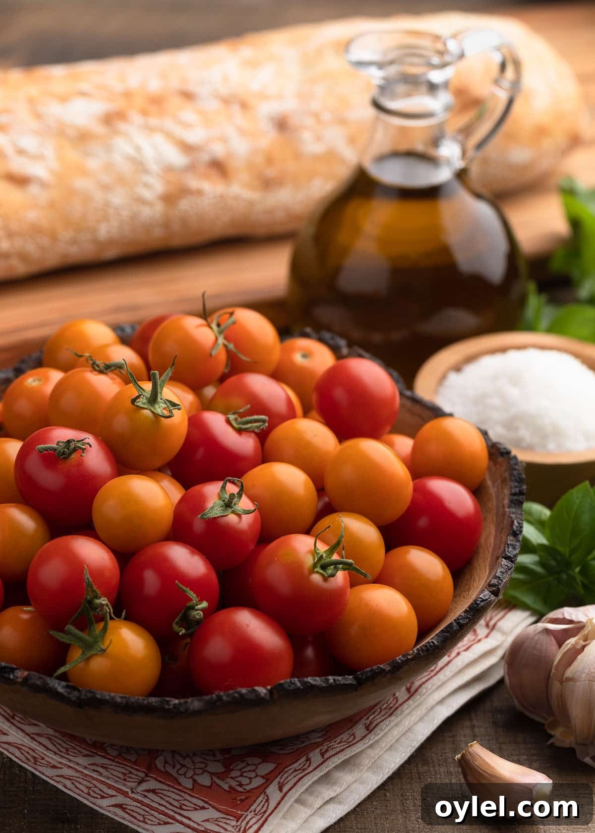 red and orange cherry tomatoes in a wood bowl, surrounded by a bowl of sea salt, a cruet of olive oil, and a loaf of ciabatta.