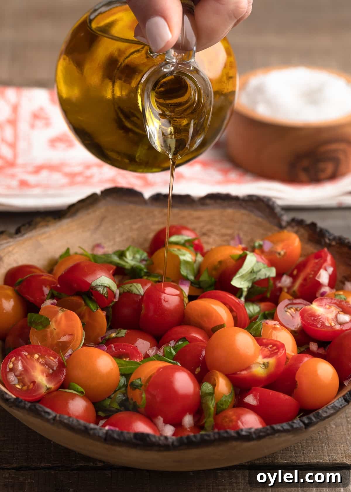pouring olive oil into a bowl of cherry tomato bruschetta topping