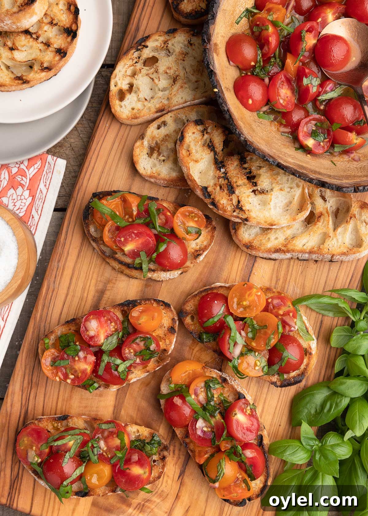 overhead photo of cherry tomato bruschetta toasts on a wooden serving board, with a bowl of tomato topping