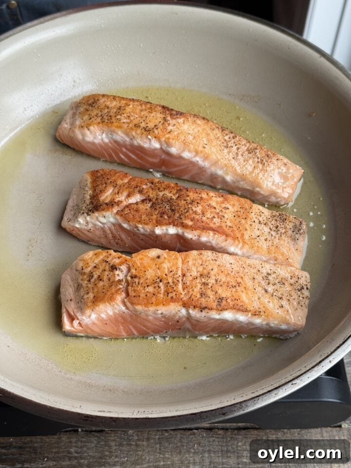 Coconut Curry Salmon in Creamy Fragrant Broth 9 a photo of three salmon fillets cooking in a pan
