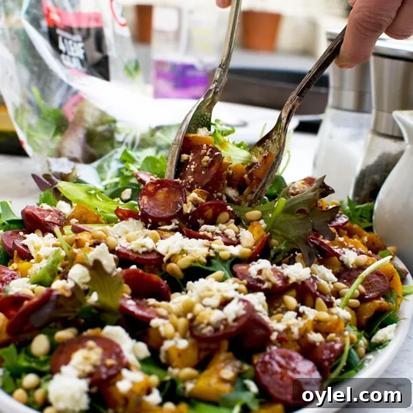 A person serving warm butternut squash, chorizo and feta salad with salad servers