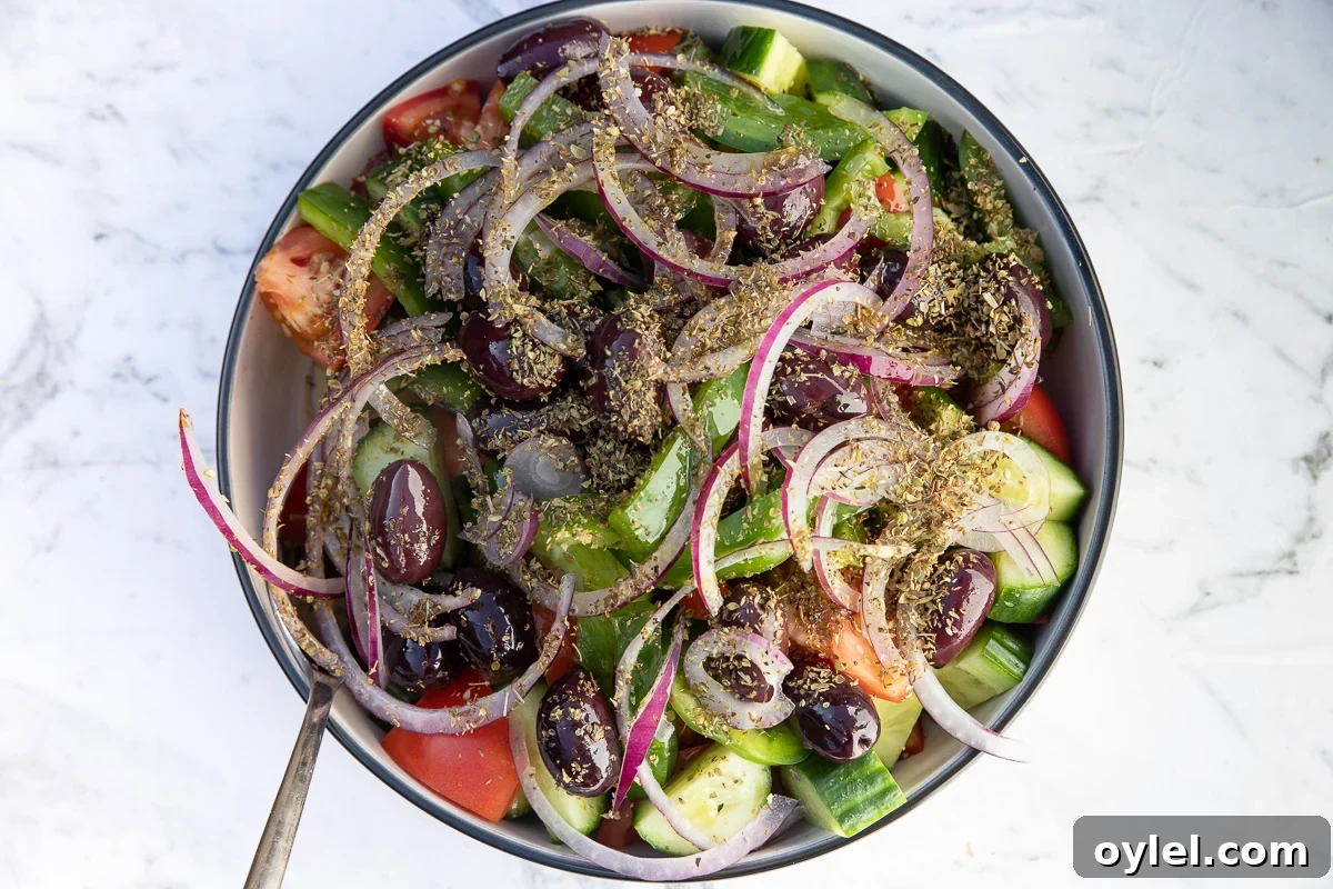 All ingredients for Greek salad apart from the feta in a big bowl with a spoon and on a marble background.