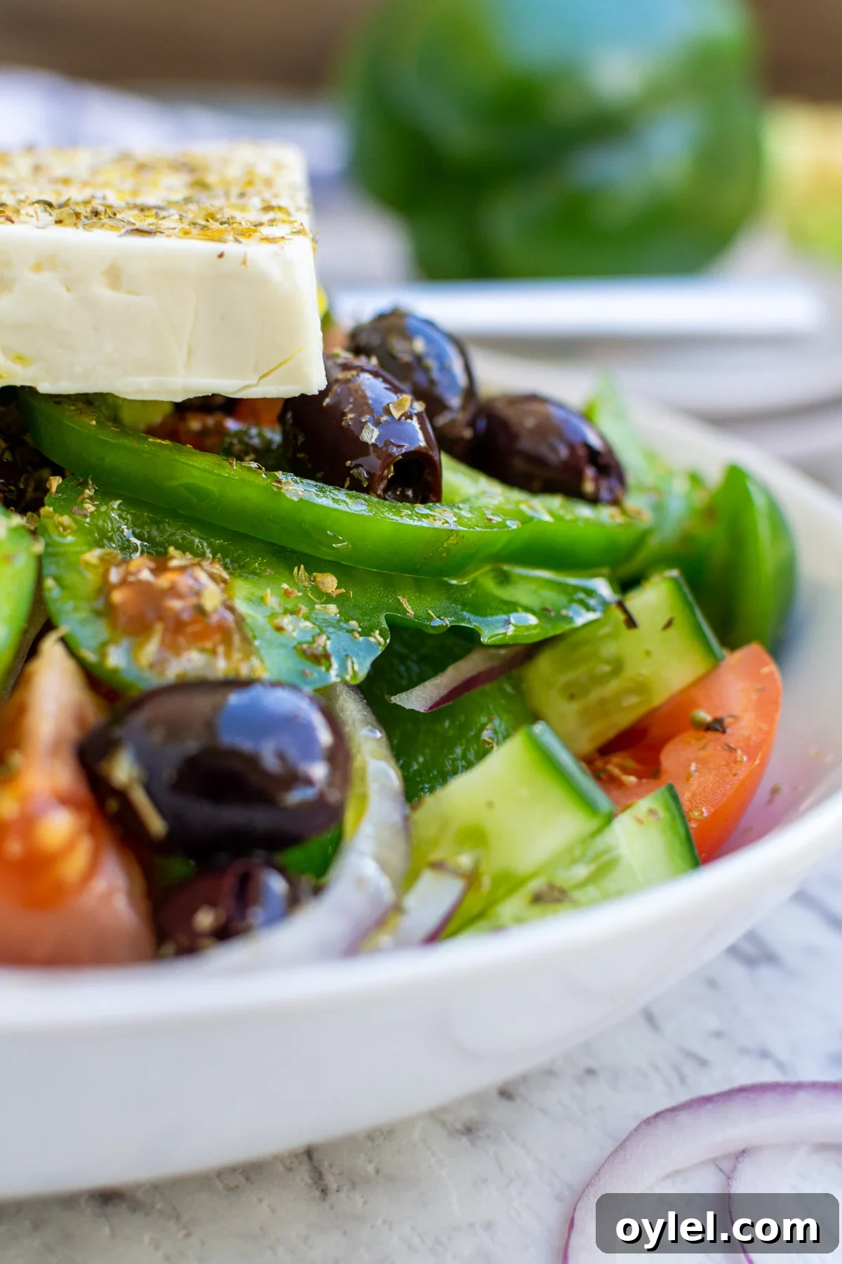 Closeup of part of a dish of traditional Greek salad in a white bowl on a marble background.