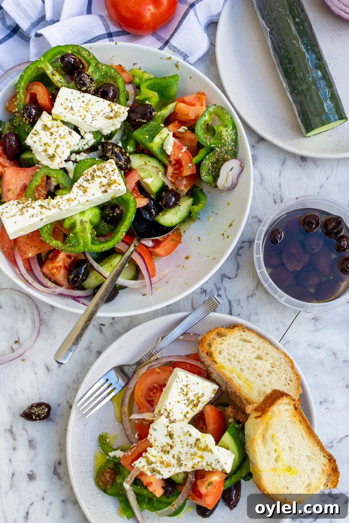 A portion of Greek salad on a plate and the rest of the salad in a bowl from above on a marble background.