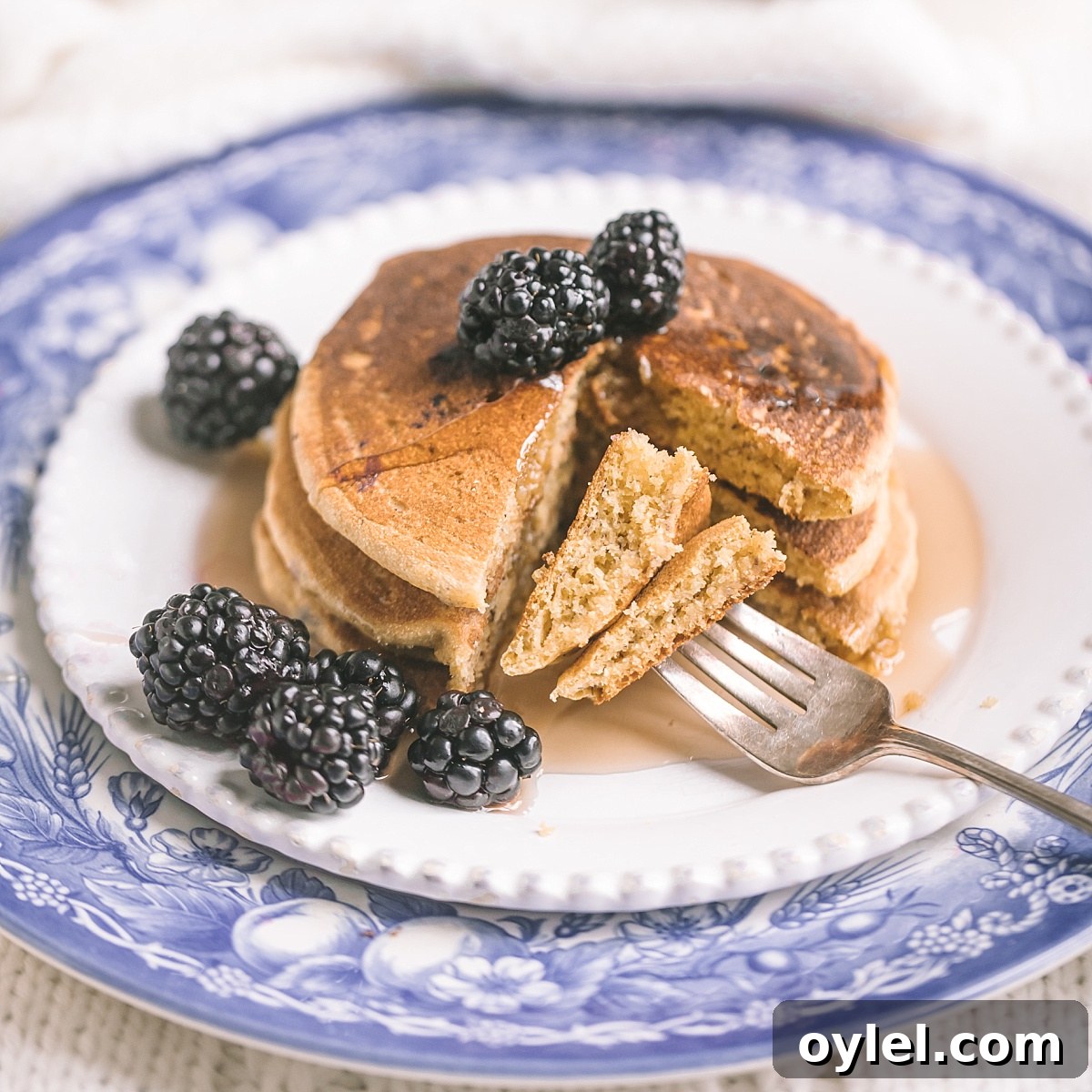 Closeup shot of fluffy, substantial but light, sweet vegan cornmeal pancakes with chunk taken out and turned on fork to show texture.