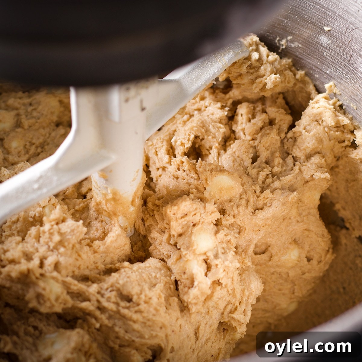 A stand mixer slowly mixing white chocolate chips into cookie dough.