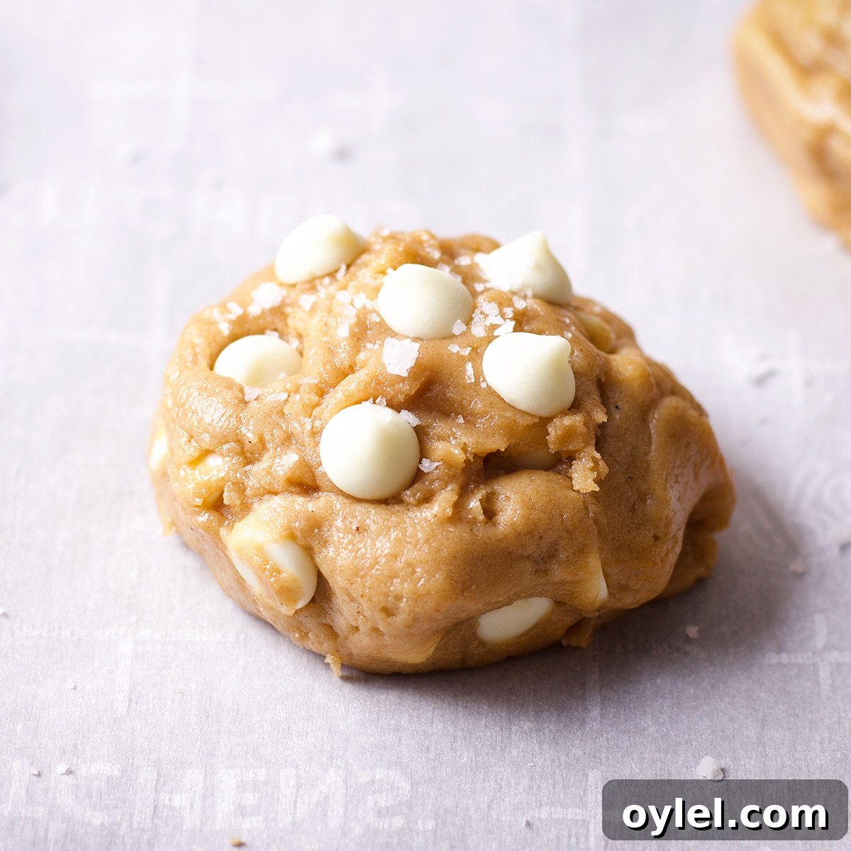 A ball of white chocolate chip cookie dough with white chocolate chips and salt pressed into the top.