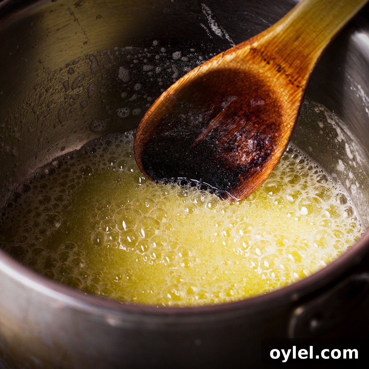 Someone using a wood spoon to stir melted, boiling butter in a saucepan.