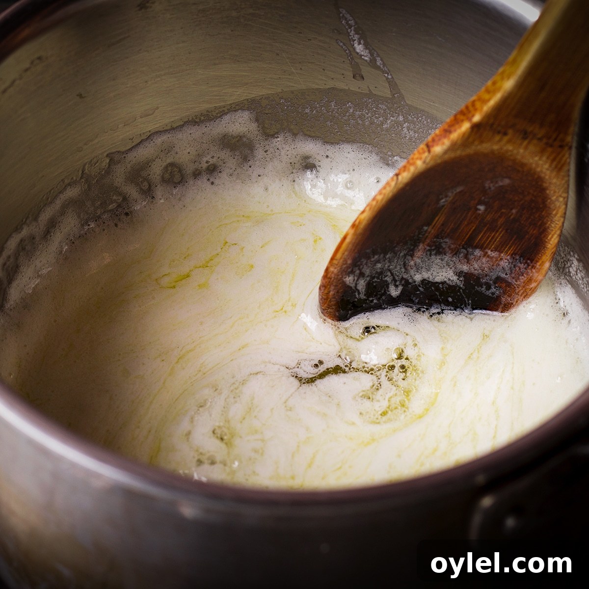 Someone using a wood spoon to stir melted butter in a saucepan. The butter is foamy and just beginning to boil.