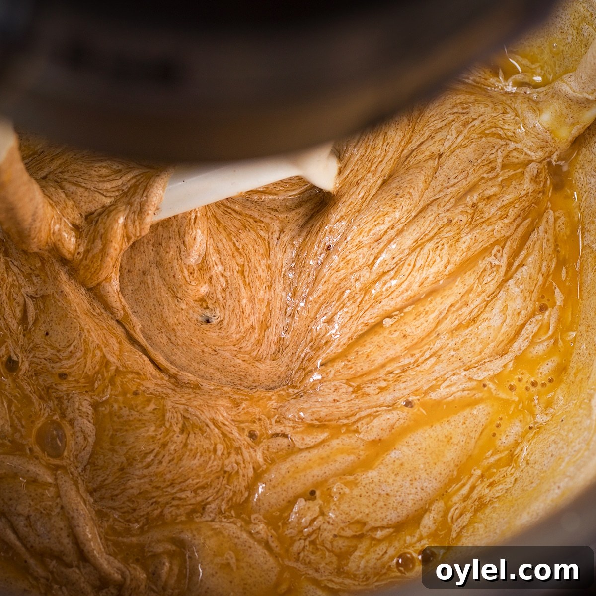 A stand mixer fitted with the paddle attachment beating eggs into cookie dough.