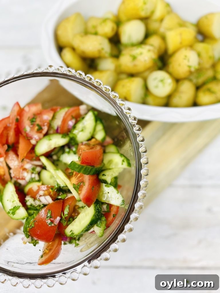Tomato and cucumber salad in a glass serving bowl next to a bowlful of Jersey Royal potatoes with butter