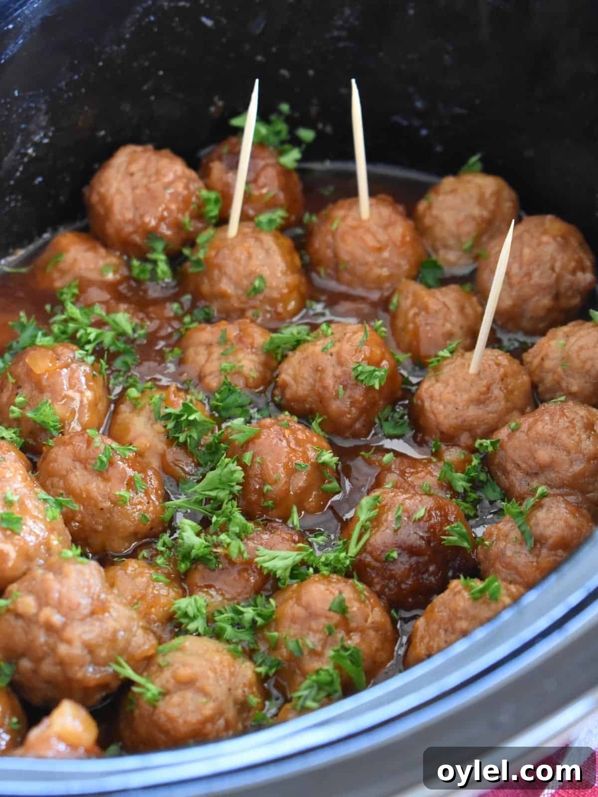 4-Ingredient Slow Cooker Hawaiian Meatballs 8 Slow Cooker Hawaiian Meatballs in a crock pot with parsley sprinkled on top and toothpicks in them.