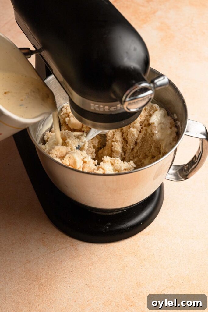 Pouring liquid into a bowl of a stand mixer full of flour mixture.