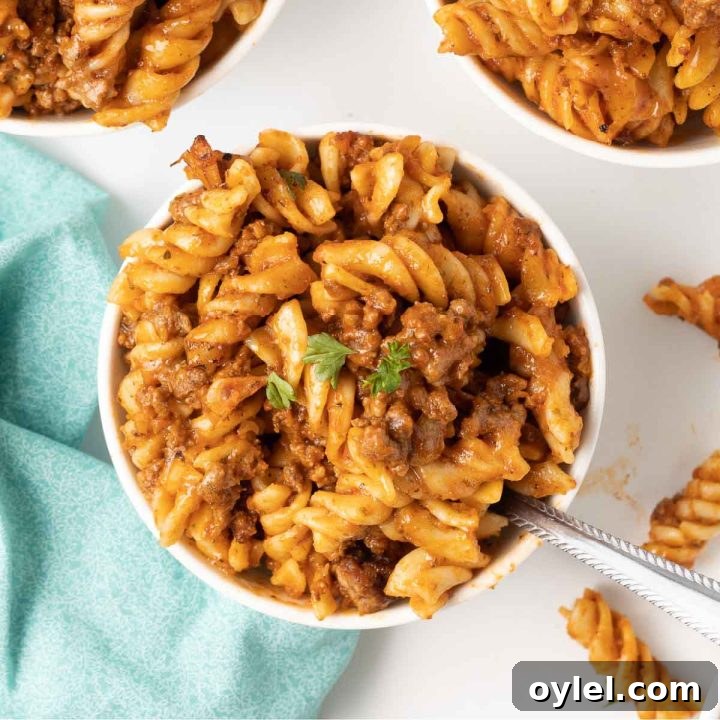 Spiral pasta bake with cheese and ground beef served in white bowls.