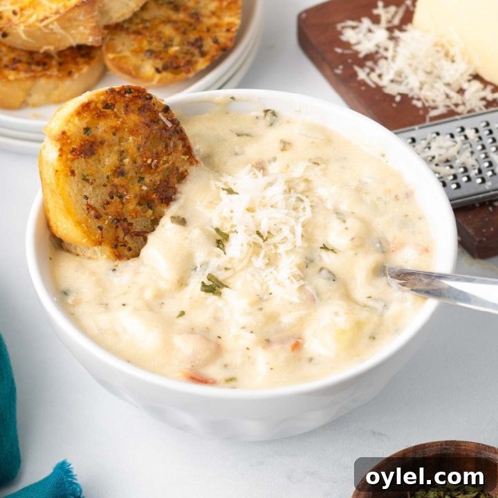 A bowl of creamy chicken and gnocchi soup served with toasted garlic bread and a wedge of Parmesan cheese.