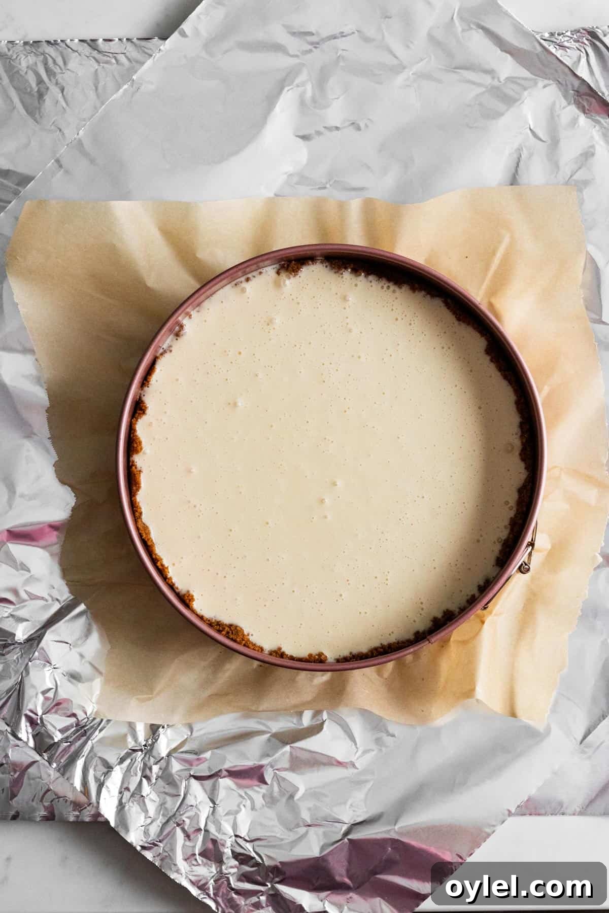 unbaked cheesecake batter in springform pan on top of 2 layers of foil