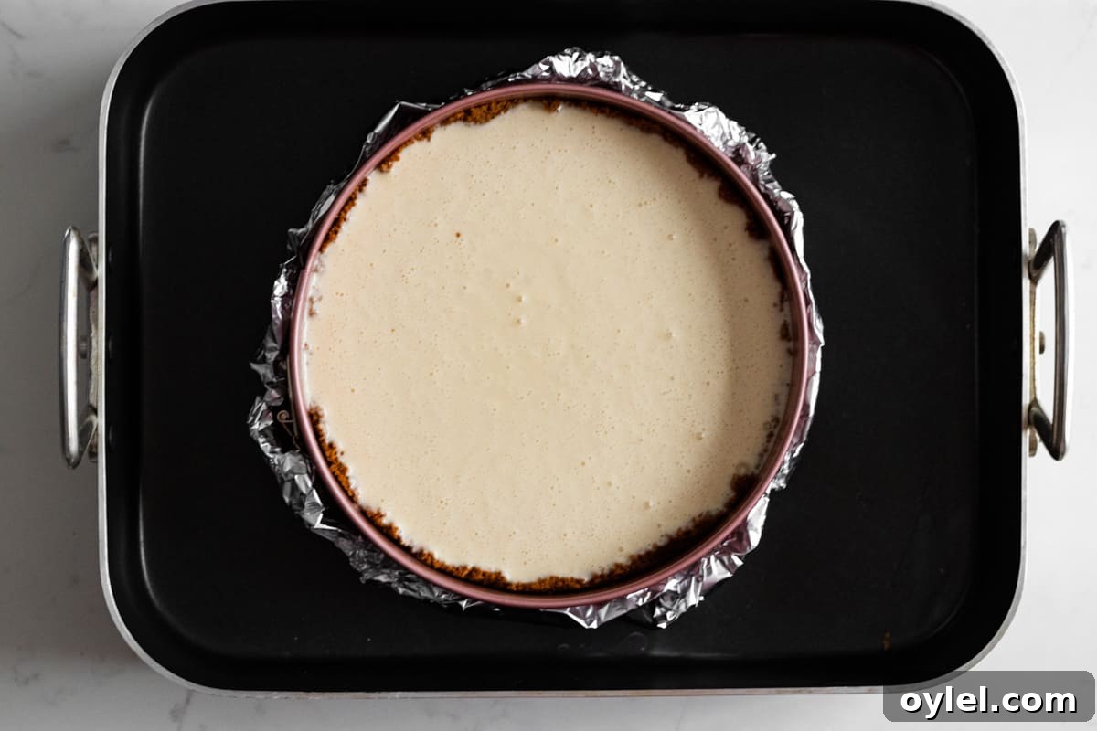 unbaked cheesecake batter in springform pan wrapped in foil and set in a roasting pan