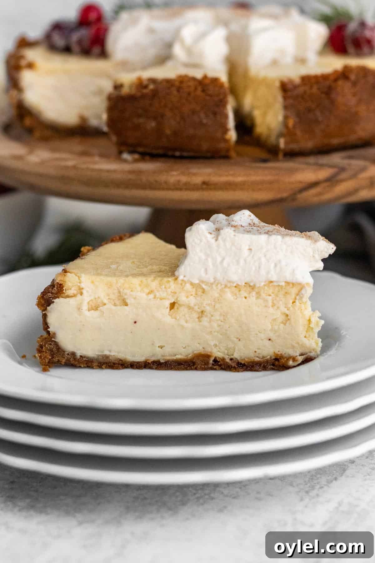 slice of eggnog cheesecake with whipped cream on a stack of white plates with the full cheesecake in the background