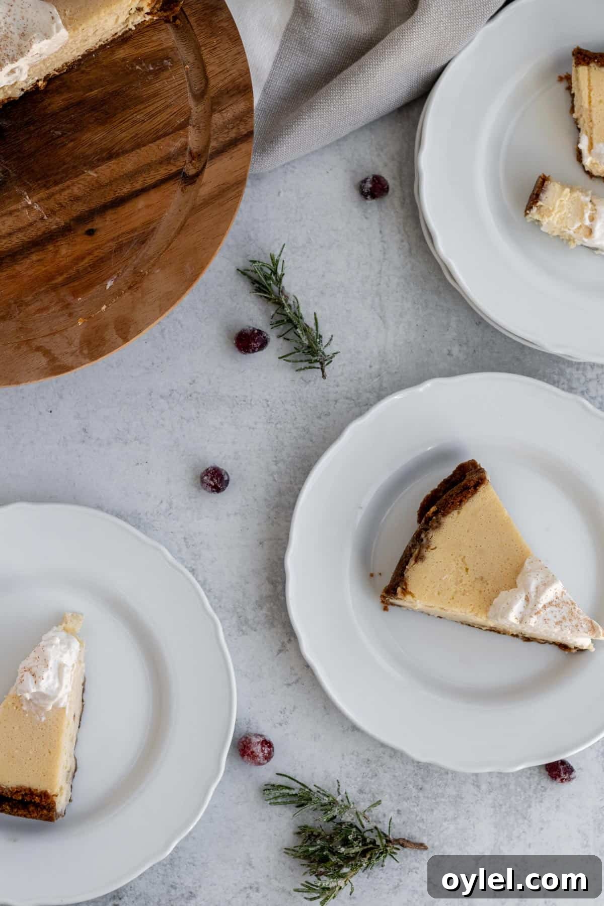 white plates with cheesecake slices on them and scattered rosemary sprigs and cranberries