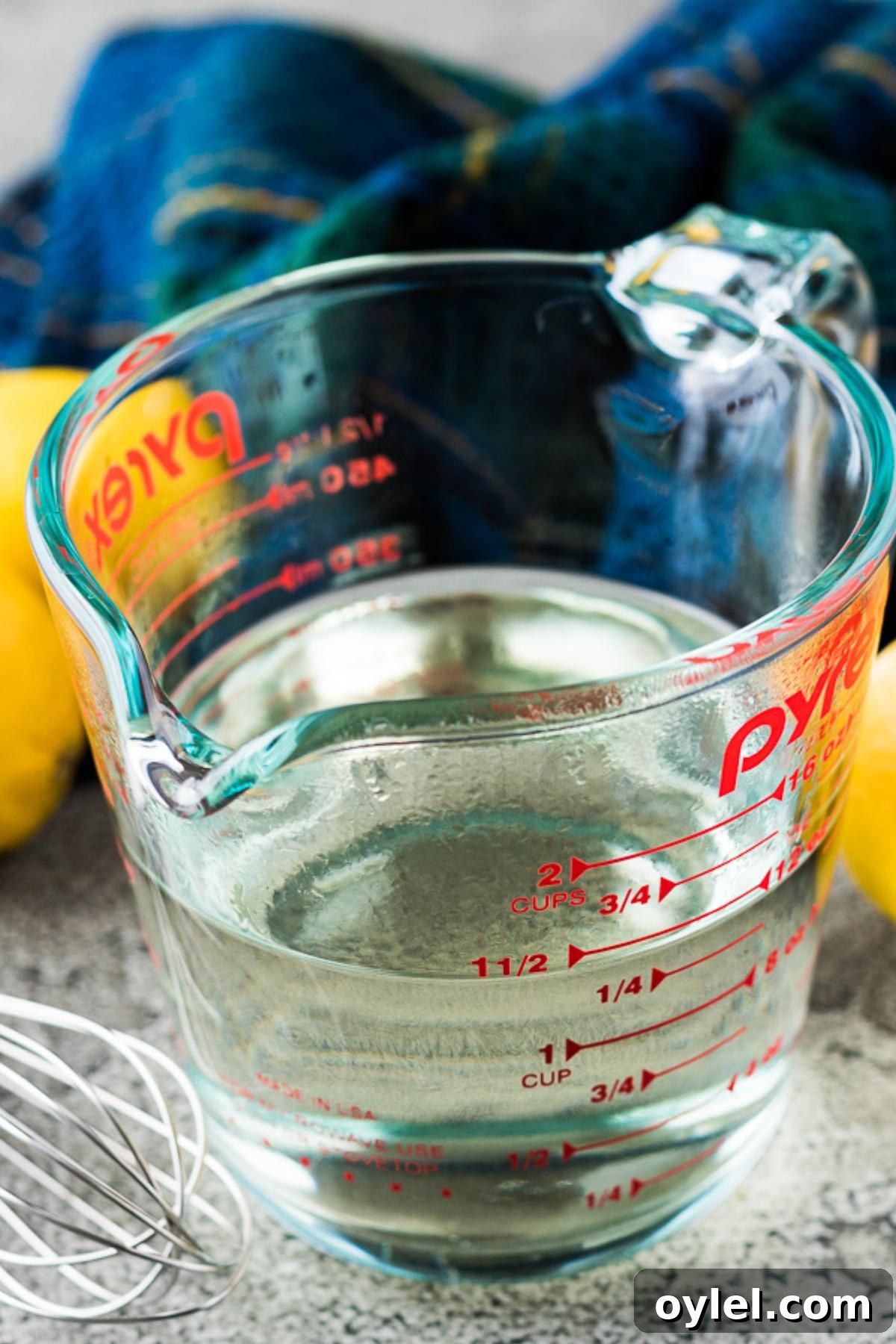 The syrup in a measuring cup surrounded by fresh lemons.