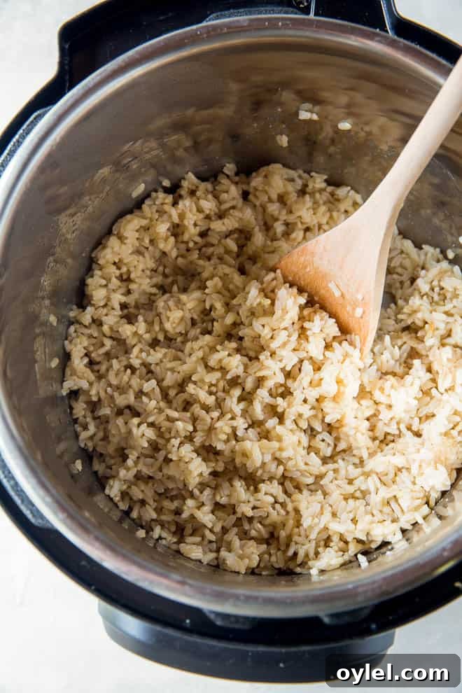 An open instant pot filled with cooked brown rice and a wooden spoon.
