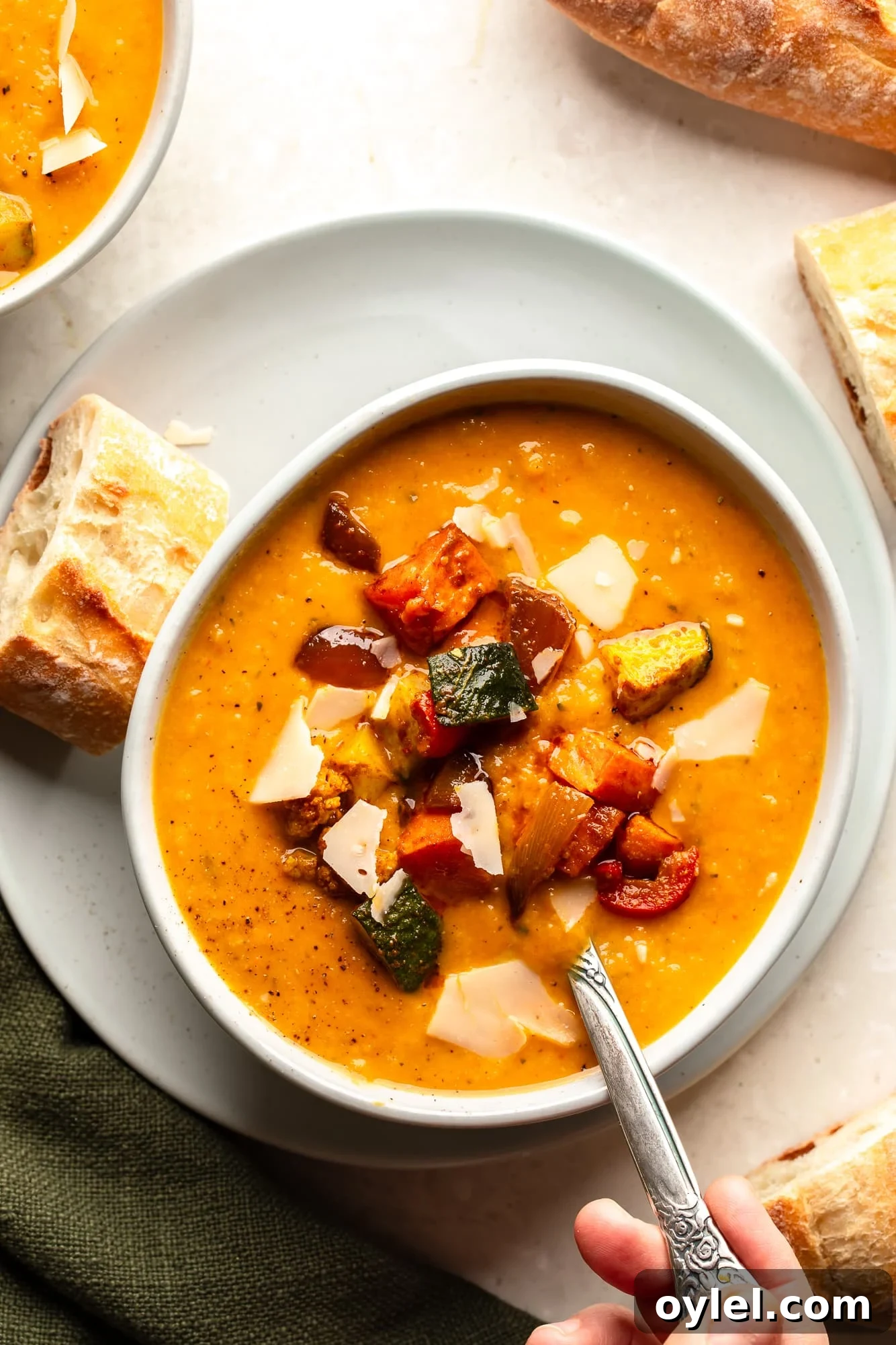 Overhead view of a bowl of roasted vegetable soup topped with roasted vegetables with a piece of bread on the side.