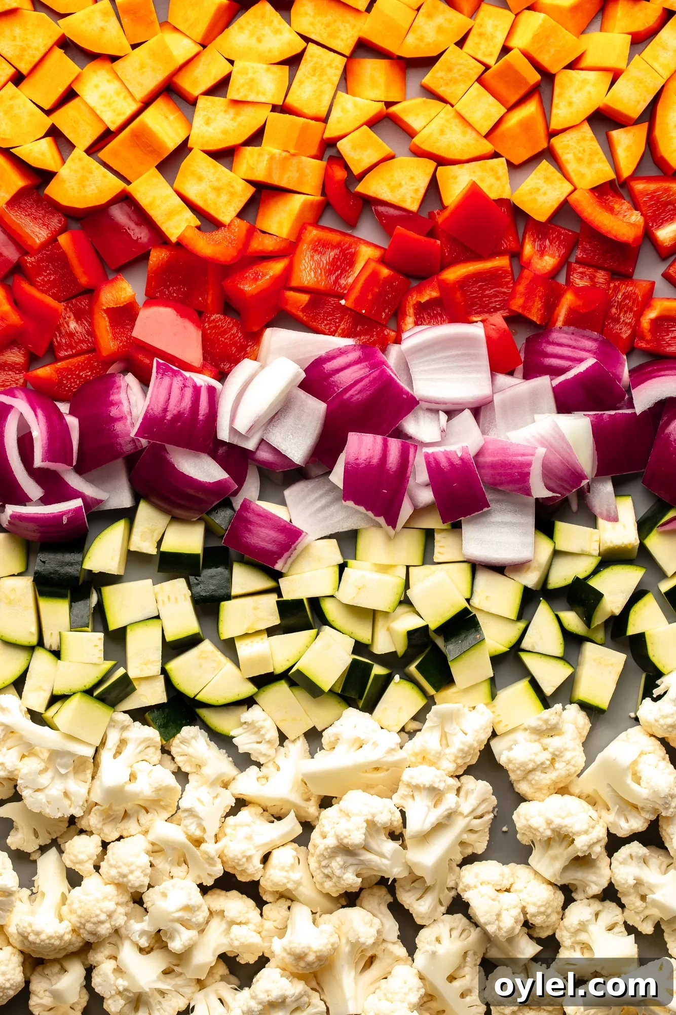 Overhead view of a medley of raw chopped vegetables on a sheet pan.