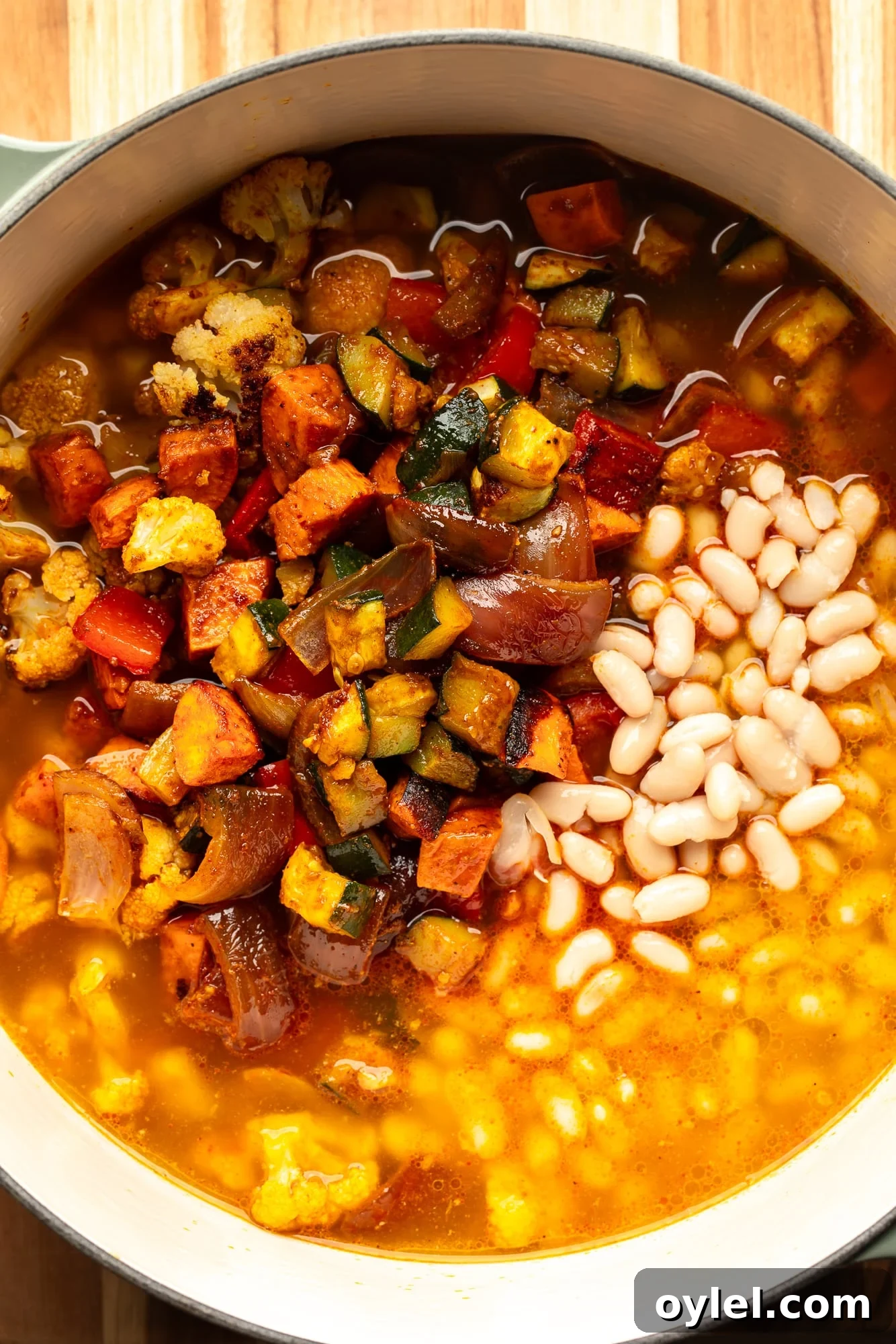 Overhead view of roasted vegetables, white beans, and broth in a large pot.