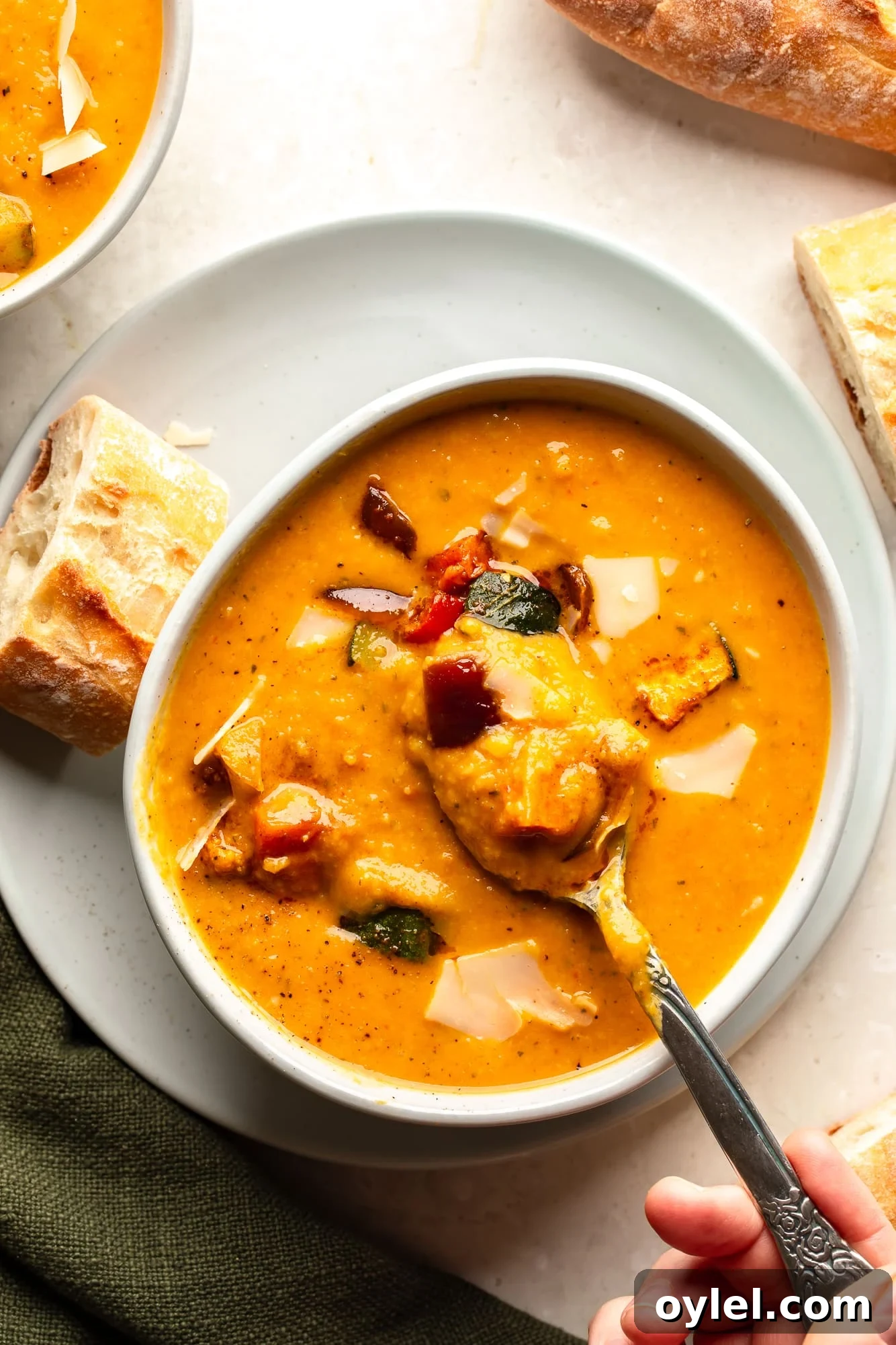 Overhead view of a woman's hand lifting a spoon out of a bowl of roasted vegetable soup.