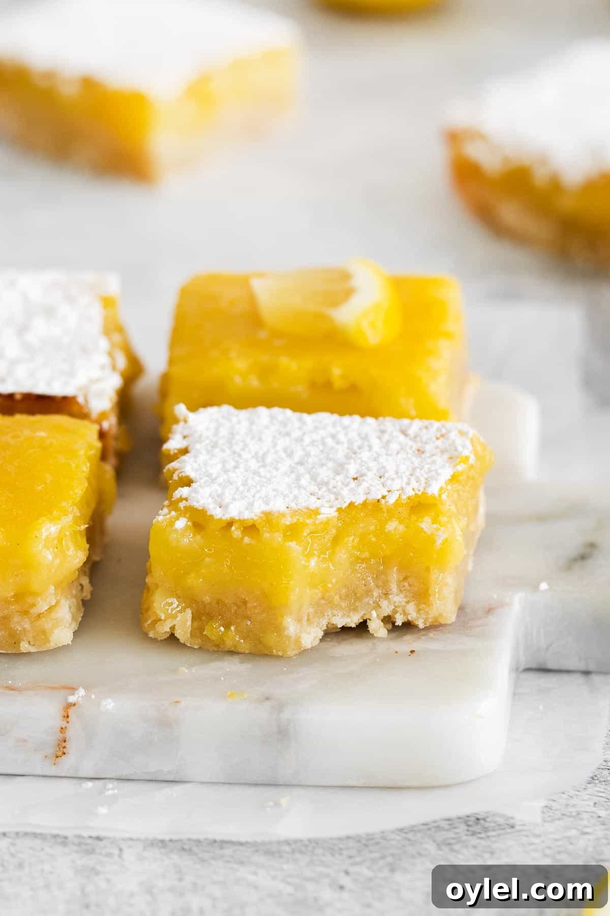 Zesty Gluten-Free Lemon Bars Recipe 3 gluten-free lemon bars on a marble platter with one bite missing.