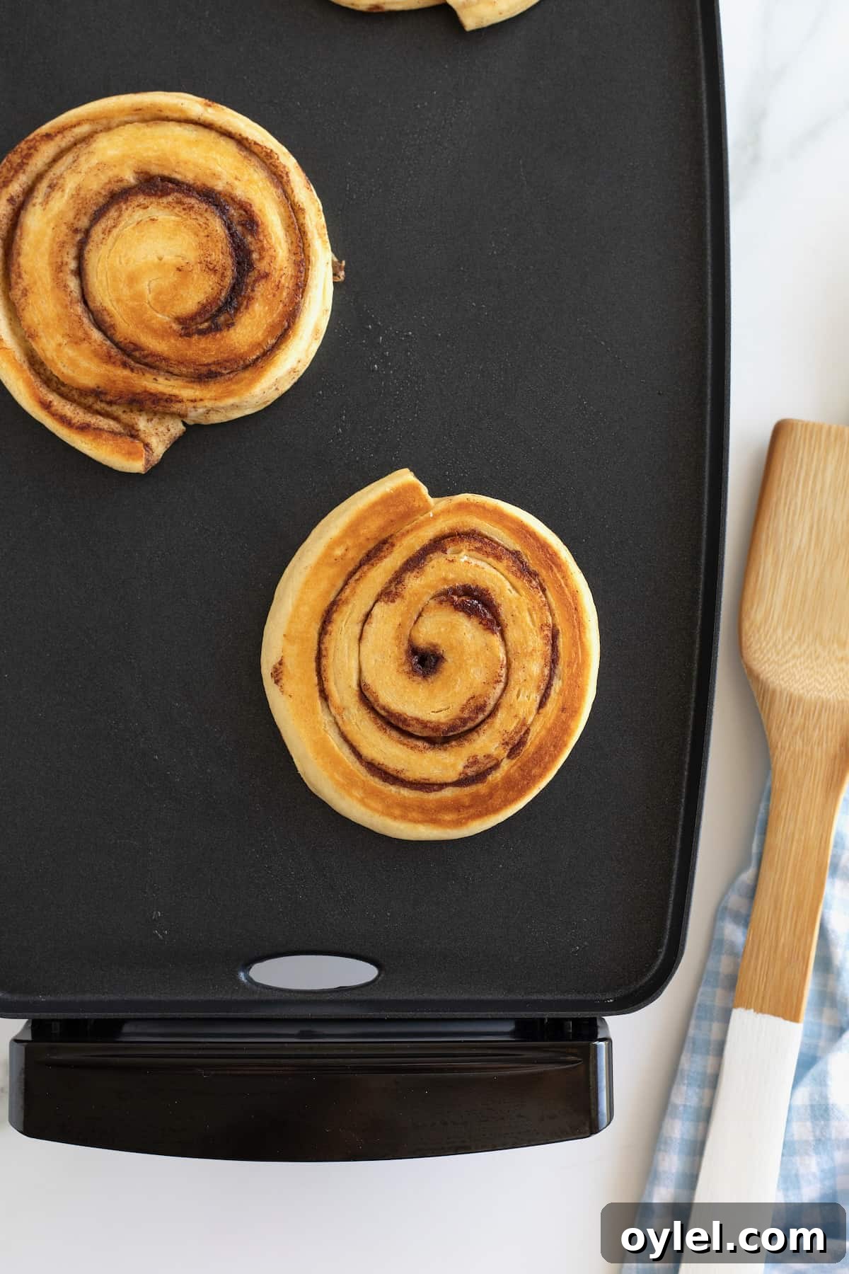 Cinnamon Roll Pancakes Recipe with Cream Cheese Glaze 3 Two cinnamon roll pancakes on a nonstick griddle.