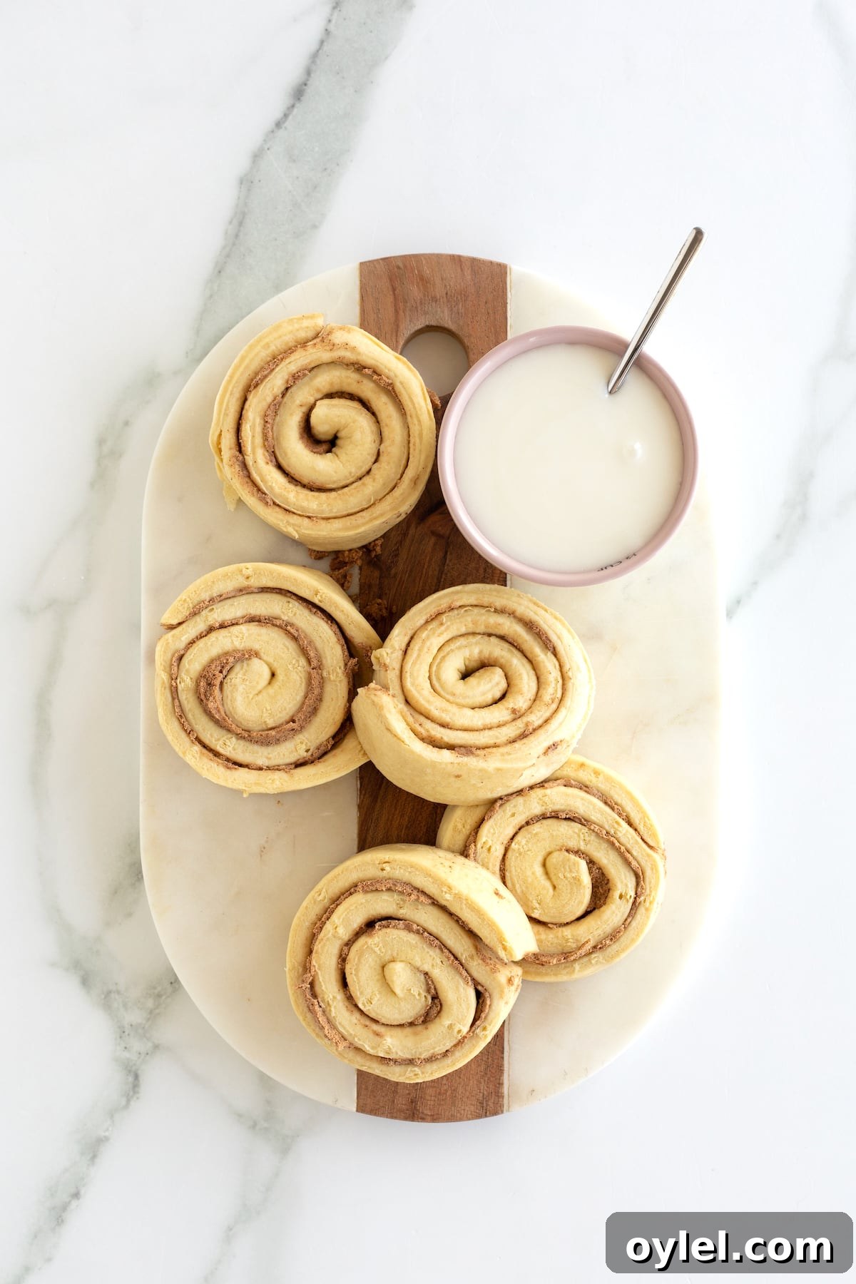 Cinnamon Roll Pancakes Recipe with Cream Cheese Glaze 5 Store bought jumbo cinnamon rolls on a cutting board with the icing on the side.