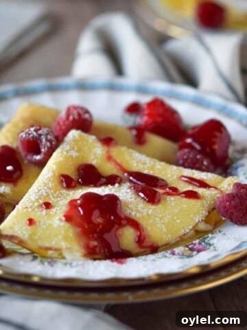 Close-up of ricotta and lemon stuffed crepes with a raspberry sauce on top.
