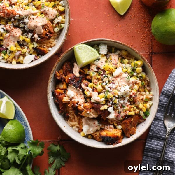 One-Pot Cajun Chicken Sausage and Rice 7 Cropped overhead photo of a street corn chicken rice bowl with grilled chicken, corn salsa, crema, Cotija cheese, and lime wedges.