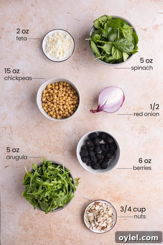 Ingredients for spinach arugula salad including feta cheese, spinach, chickpeas, red onion, arugula, berries, nuts.
