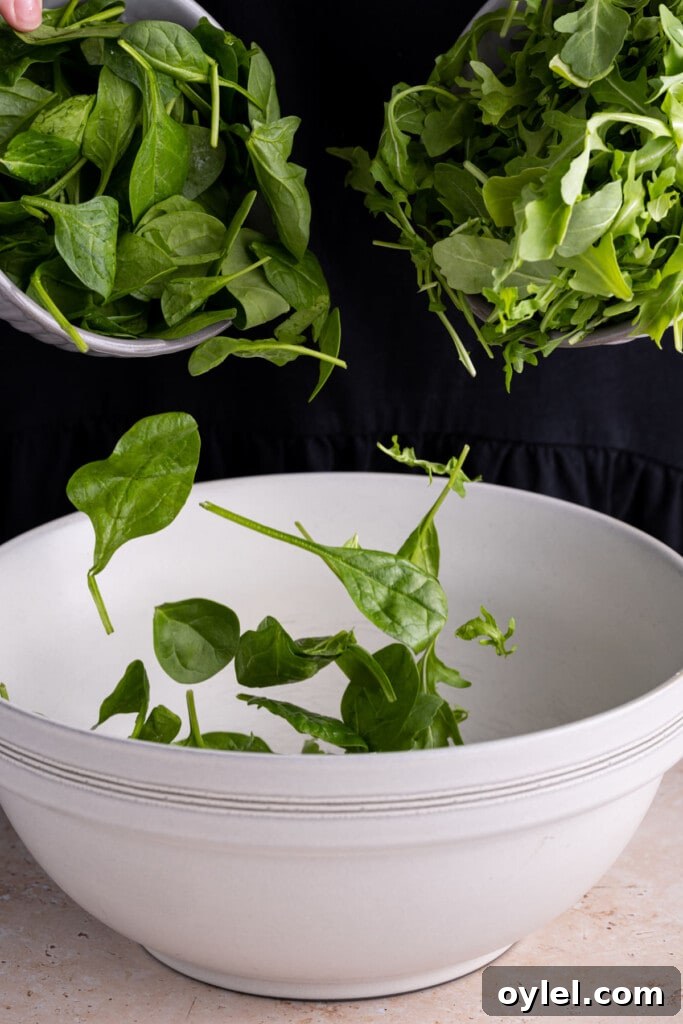 Adding spinach and arugula together in a large mixing bowl.