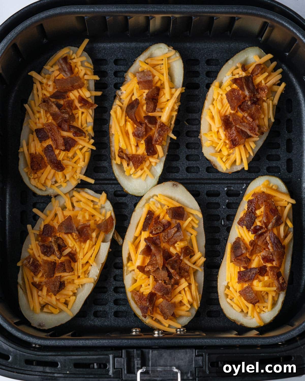 Crispy Air Fryer Potato Skins with Cheese and Bacon 7 uncooked potato skins in air fryer basket.