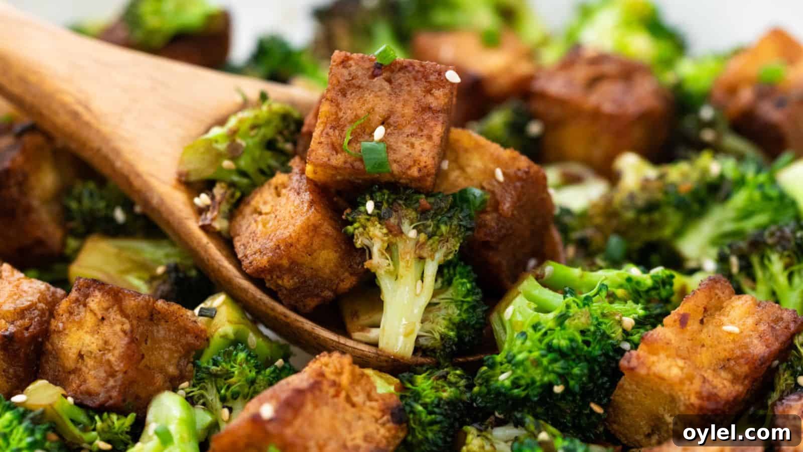 13 Asian Recipes You Won't Believe Are This Simple 11 Close-up of roasted broccoli and tofu cubes tossed with sesame seeds in a wooden spoon, set against a blurred background.